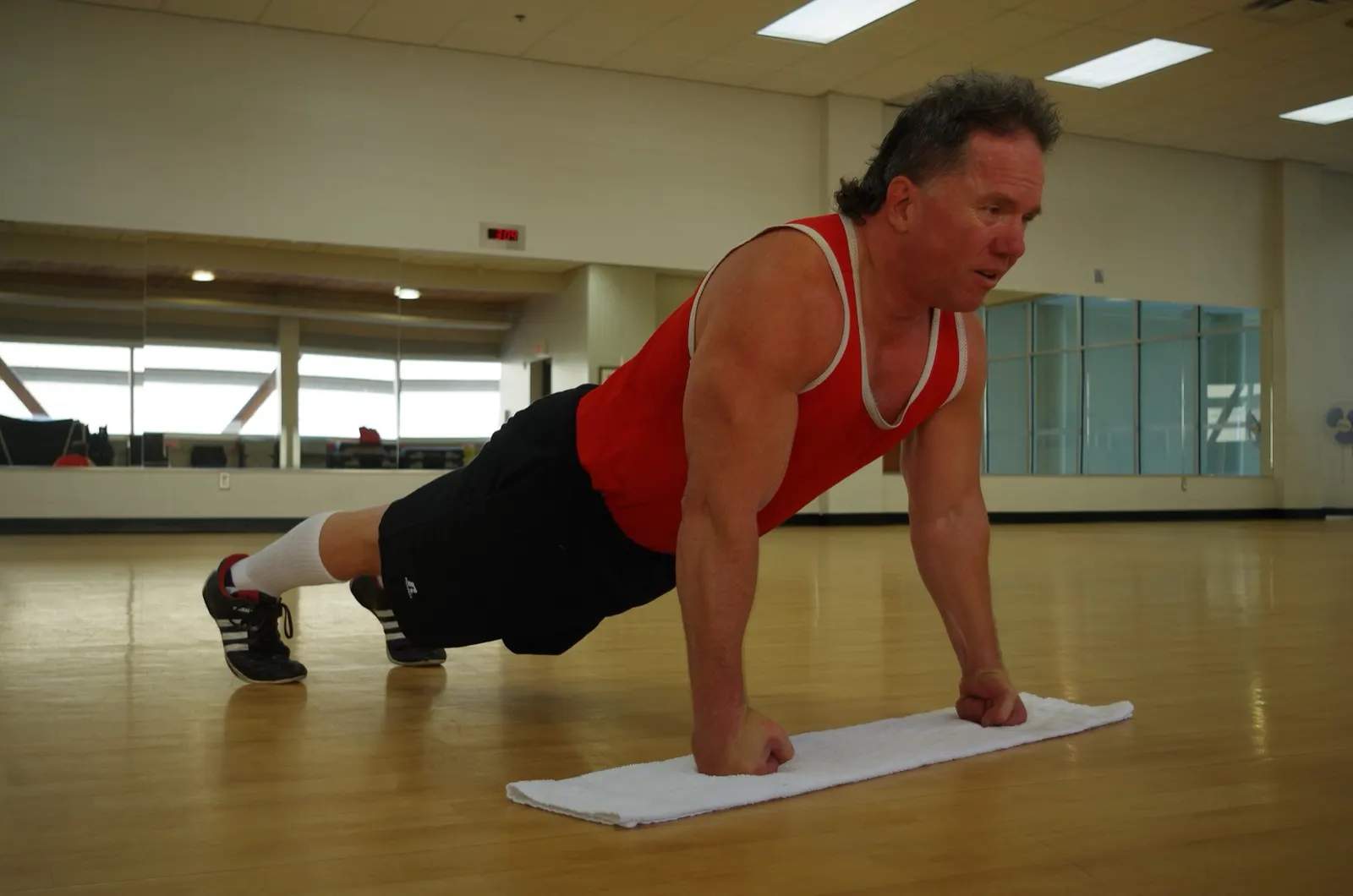 Doug Pruden doing knuckle push-ups in Edmonton, 2015; photographer Doug Pruden; CC BY-SA 4.0. Original page: https://commons.wikimedia.org/wiki/File:Doug_Pruden_knuckle_push_ups.JPG. Attribution: Doug Pruden, CC BY-SA 4.0, via Wikimedia Commons. License: https://creativecommons.org/licenses/by-sa/4.0/. Resized to 1800 px maximum dimension and saved as JPEG quality 88; no crop. This is a separate fist-supported push-up variation, not the back-of-hands form.