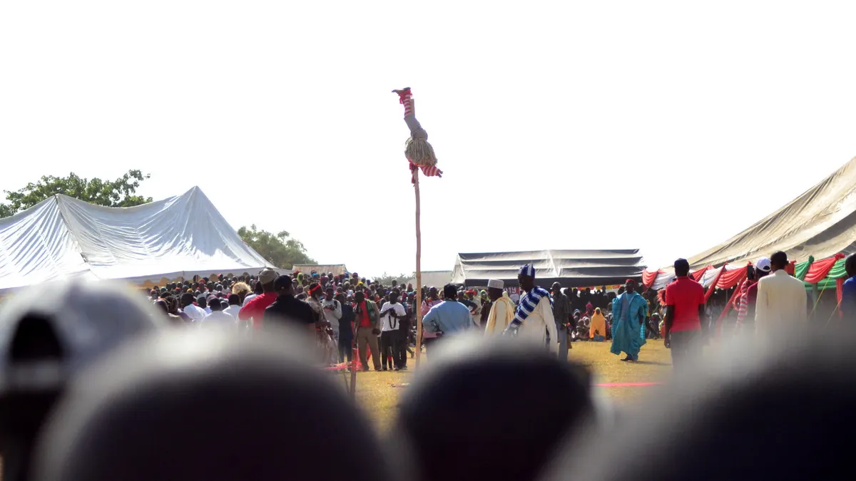 pole acrobat performing upside down above a crowd; photographer Dotun55; CC BY-SA 4.0. Original: https://commons.wikimedia.org/wiki/File:Pole_Acrobat_2.jpg. Attribution: Dotun55, CC BY-SA 4.0, via Wikimedia Commons. Visually inspected 2026-10-18.