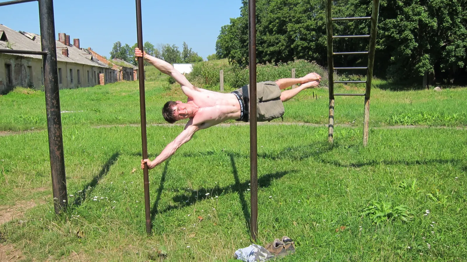a different athlete performing a human flag between bars in Daugavpils, Latvia, photographed 2012; creator Romans Janovics (Commons username Romkincom); CC BY-SA 3.0 or GFDL. Original file page: https://commons.wikimedia.org/wiki/File:Human_Flag_by_Romans_Janovics_in_Daugavpils,_Latvia.jpg. Attribution: Romans Janovics, CC BY-SA 3.0, via Wikimedia Commons. License: https://creativecommons.org/licenses/by-sa/3.0/. Resized to 1800 px maximum dimension and saved as JPEG quality 88; no crop.