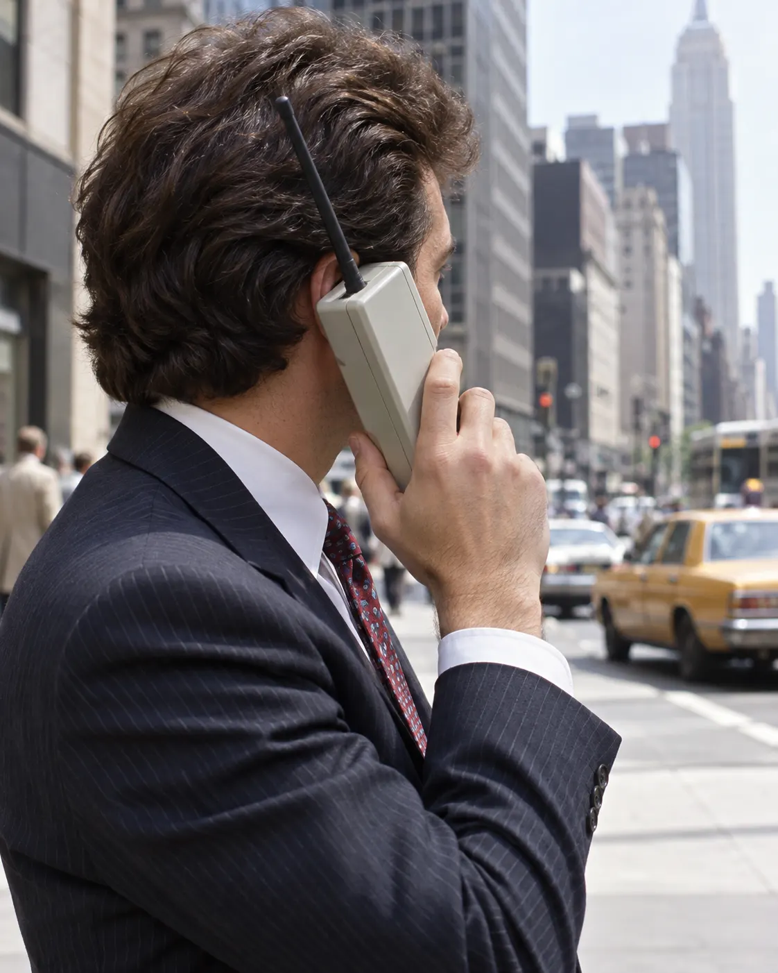 AI-generated historical reconstruction of an anonymous person using a generic early 1980s mobile phone; not Martin Cooper or a documentary scene. Prompt: “Photorealistic editorial image of an anonymous person using an early 1980s handheld mobile phone outdoors, large portable handset, city street in the background, vertical 4:5. Historically inspired generic reconstruction, no recognizable real individual, brand labels, legible text, or claim to depict Martin Cooper.” Generated 2026-10-19.