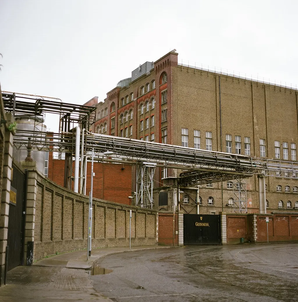 Guinness brewery buildings and gate in Dublin; photographer Andrius Burlega; CC BY-SA 3.0. Original page: https://commons.wikimedia.org/wiki/File:Guinness_brewery_Dublin.JPG. Attribution: Andrius Burlega, CC BY-SA 3.0, via Wikimedia Commons; license: https://creativecommons.org/licenses/by-sa/3.0/.