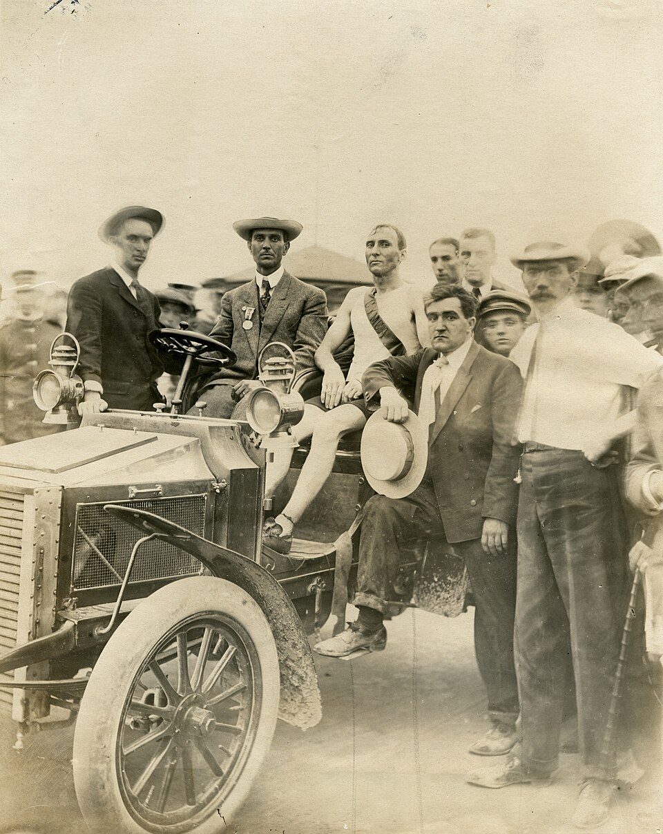 Documentary photo of Hicks resting in a car after the race, photographed by Jessie Tarbox Beals; Missouri History Museum collection via Wikimedia Commons, Public Domain Mark 1.0. https://commons.wikimedia.org/wiki/File:1904_Olympics-_Thomas_J._Hicks,_Boston,_winner_of_the_Marathon_Race_resting_in_a_car_after_the_finish.jpg