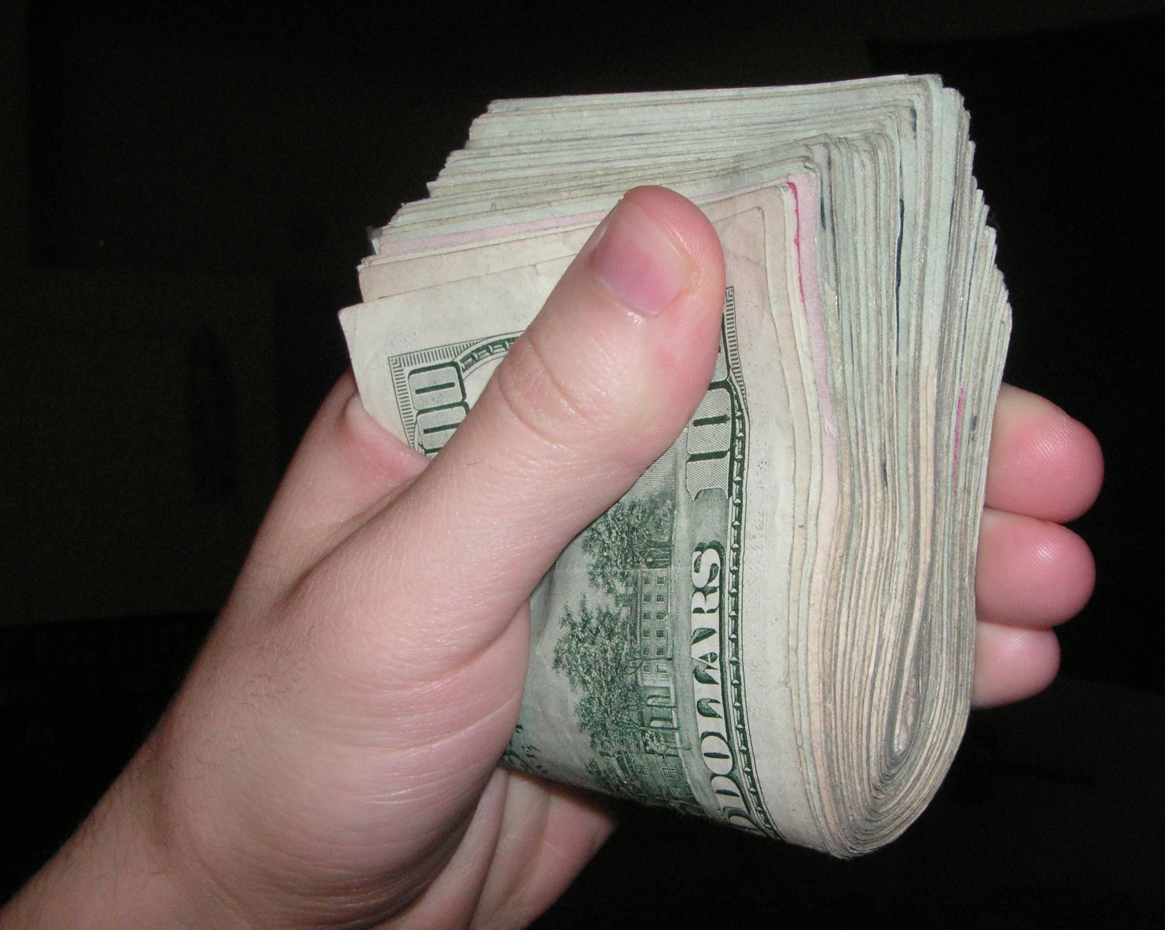 hand holding a thick stack of genuine U.S. notes, not movie props; creator Psychonaught (page later revised by Reworked); public-domain dedication; original https://commons.wikimedia.org/wiki/File:American_Cash.JPG