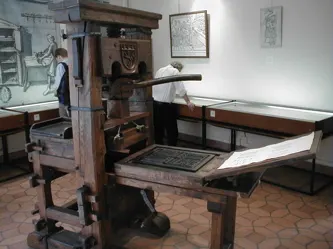 photograph of a reconstructed Gutenberg-era press on display at the Printing History Museum, Lyon; Wikimedia Commons file page identifies the depicted object as a reproduction; uploader Ghw released the photograph into the public domain. https://commons.wikimedia.org/wiki/File:Gutenberg.press.jpg. Labeled as a reconstruction, not Gutenberg’s surviving original.