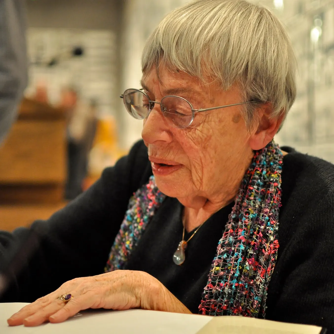 documentary photo of Ursula K. Le Guin signing a book, 6 Jan 2013. Photographer K. Kendall. Original page: https://commons.wikimedia.org/wiki/File:Ursula_Le_Guin.jpg. CC BY 2.0; attribution “K. Kendall / Wikimedia Commons / CC BY 2.0”; no edits; visually checked.