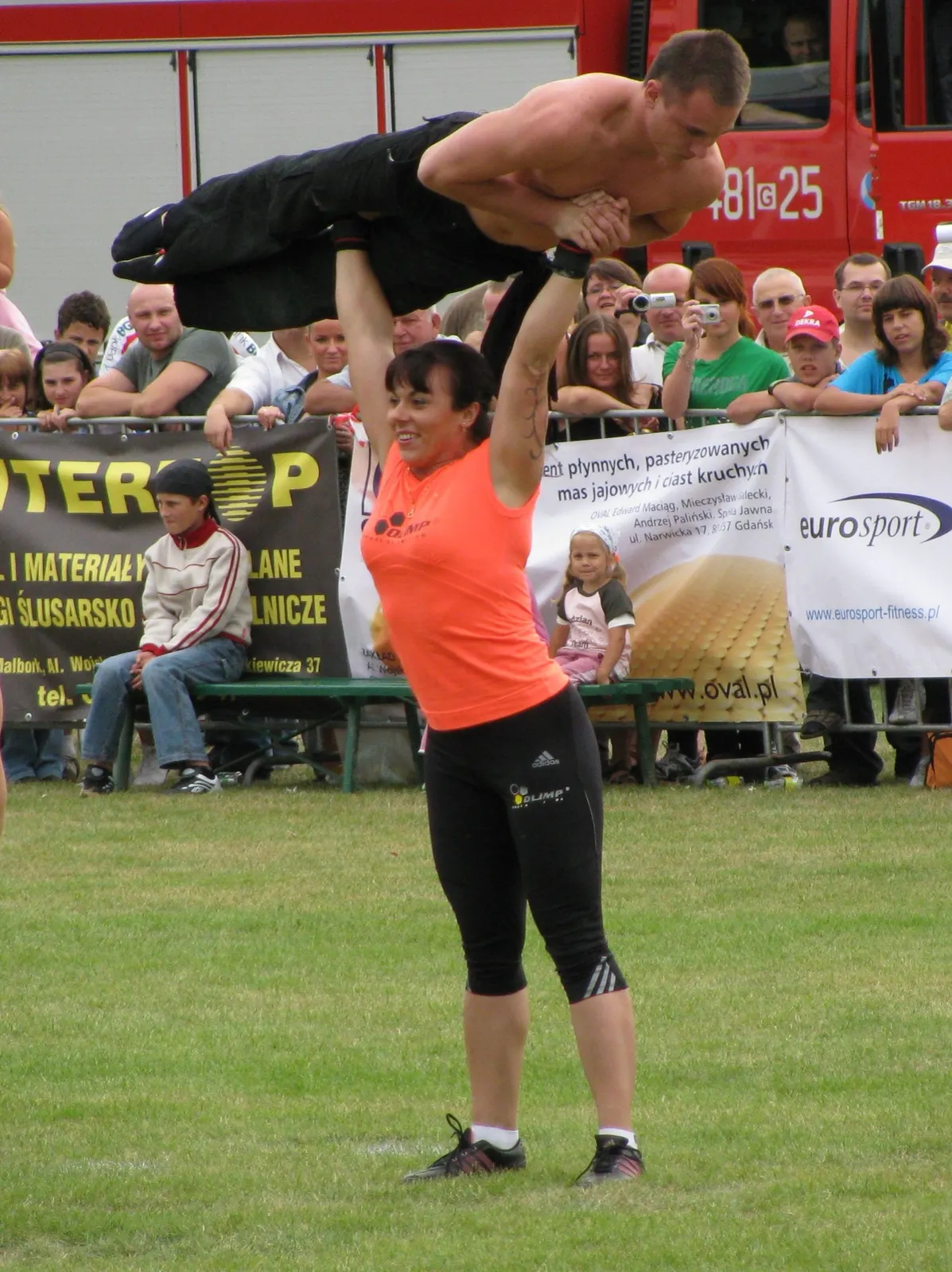 Aneta Florczyk lifting a man overhead at a public event in 2009; photographer Artur Andrzej; CC BY-SA 3.0. Original page: https://commons.wikimedia.org/wiki/File:Aneta_Florczyk2.JPG. Attribution: Artur Andrzej, CC BY-SA 3.0, via Wikimedia Commons. License: https://creativecommons.org/licenses/by-sa/3.0/. Resized to 1800 px maximum dimension, JPEG quality 88; no crop.