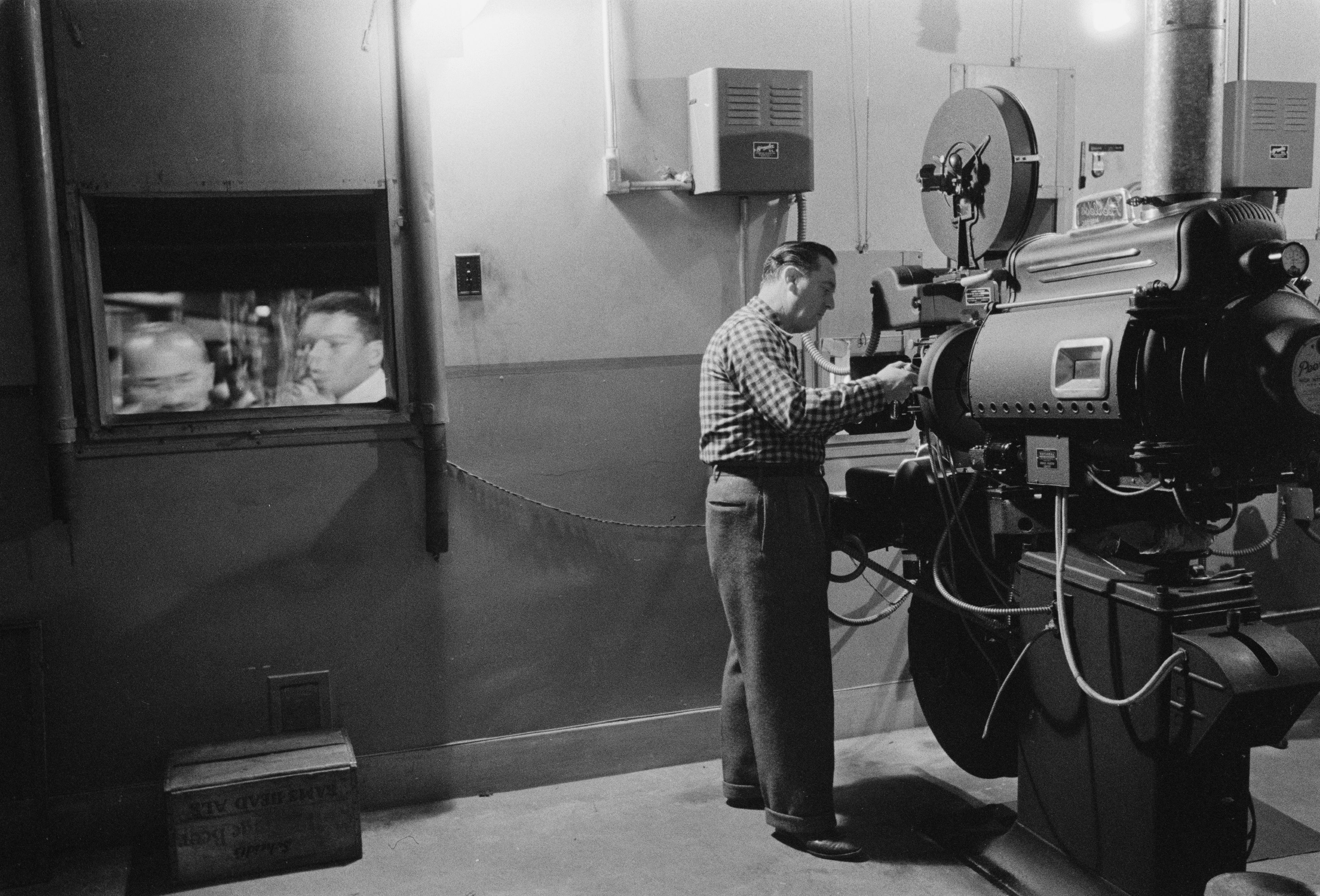 projectionist operating cinema equipment in 1958; photograph Marion S. Trikosko, Library of Congress; no known copyright restrictions per LoC; attribution “Marion S. Trikosko, U.S. News & World Report Magazine Photograph Collection, Library of Congress”; unchanged. Original: https://commons.wikimedia.org/wiki/File:Man_working_with_a_projector_in_a_movie_theater_1958.jpg