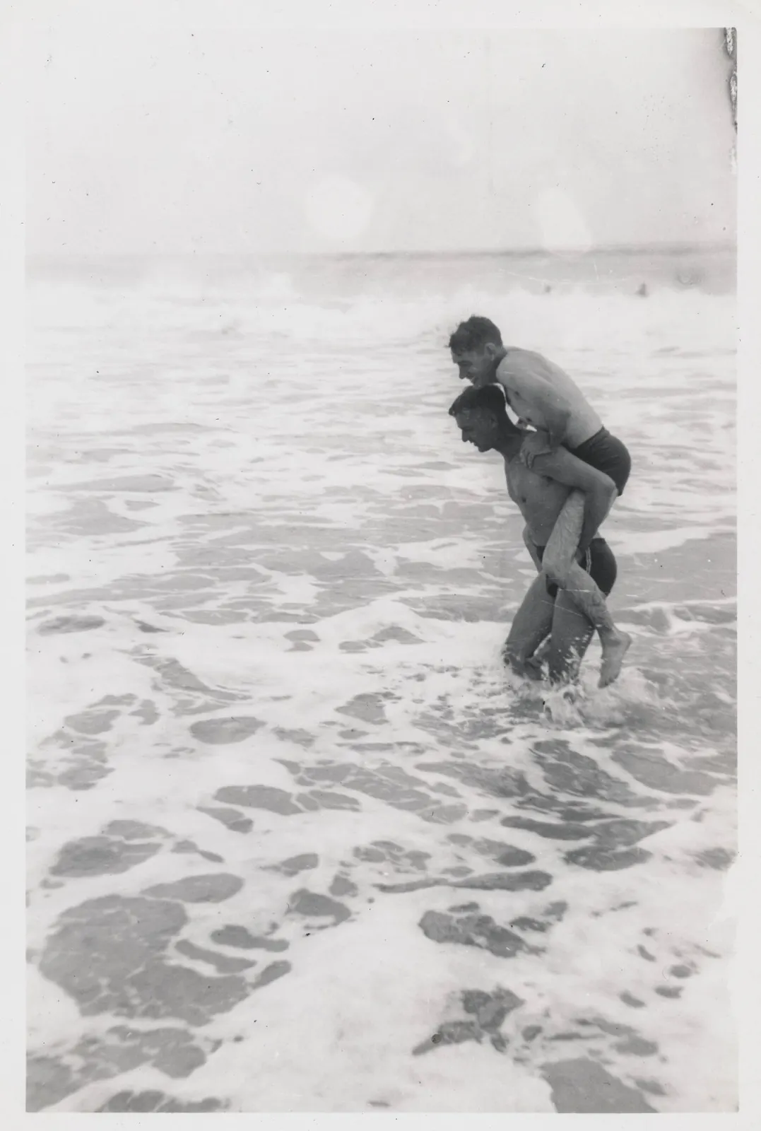 documentary photograph of two men playing piggyback in the surf, by simpleinsomnia; CC BY 2.0. Original: https://commons.wikimedia.org/wiki/File:Two_men_play_piggyback_in_the_surf_(10361985535).jpg. Attribution: simpleinsomnia, CC BY 2.0, via Wikimedia Commons. Resized to fit 1800 px and saved as optimized JPEG quality 88.