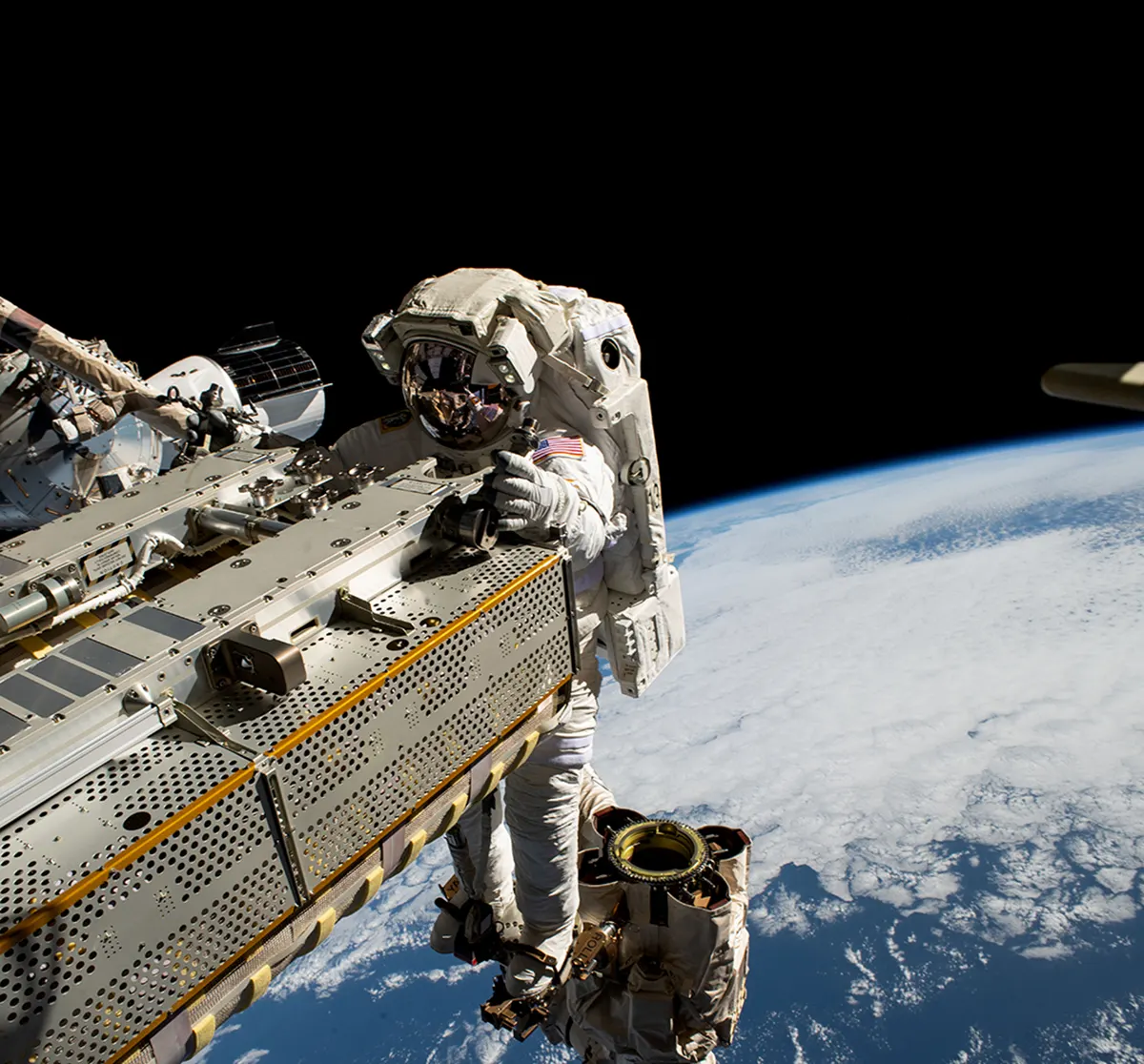 NASA photo ISS069E018537 of astronaut Woody Hoburg on a spacewalk using Canadarm2. Source: NASA Spinoff, https://spinoff.nasa.gov/sites/default/files/2023-08/iss069e018537_web.jpg. NASA credit; public-domain US federal government work. The photograph is contextual and does not purport to show the MAG beneath the suit.