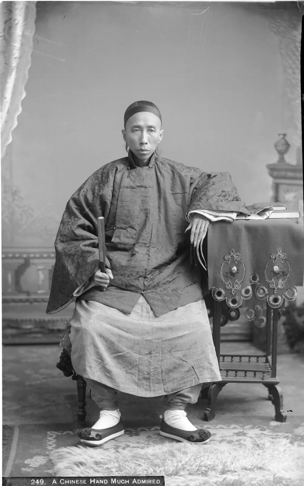 a second archival studio portrait of the same unidentified Chinese doctor, circa 1920, with long fingernails visible. Photographer C. C. Pierce. The USC Digital Library/California Historical Society item is marked public domain on Wikimedia Commons. Attribution: C. C. Pierce / California Historical Society Collection, USC Libraries Special Collections; public domain. No edits. [Original asset page](https://commons.wikimedia.org/wiki/File:Chinese_doctor_with_long_finger_nails_(an_aristocrat),_ca.1920_(CHS-249).jpg).