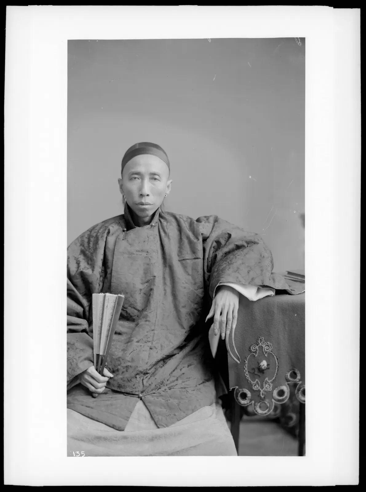archival portrait of a Chinese doctor showing exceptionally long fingernails on his left hand, circa 1895–1920. Photographer C. C. Pierce. The USC Digital Library/California Historical Society item is marked public domain on Wikimedia Commons. Attribution: C. C. Pierce / California Historical Society Collection, USC Libraries Special Collections; public domain. No edits. [Original asset page](https://commons.wikimedia.org/wiki/File:Chinese_doctor_with_long_finger_nails,_ca.1895-1920_(CHS-135).jpg).